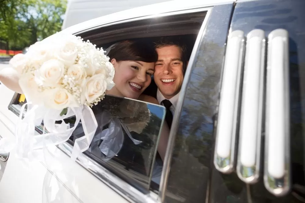 Portrait Of Newlywed Couple Smiling Sitting In Limousine Holding Bouquet In Hand.